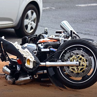A motorcycle lies on the ground beside a car, indicating a recent motorcycle accident on the roadway - Brian Moore Injury Law
